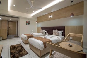 Une chambre d’hôtel avec deux lits, un ventilateur de plafond, une petite table et un luminaire fixé au mur.