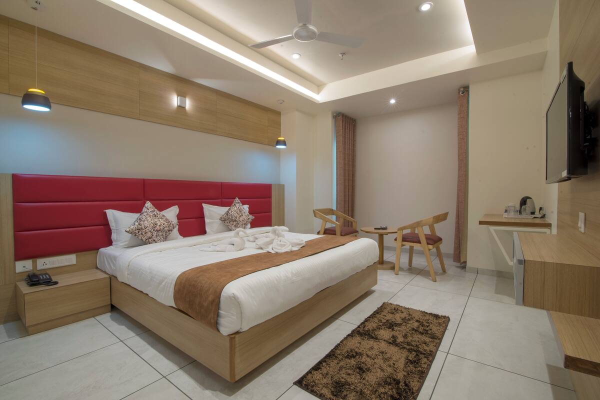 Ein modernes Hotelzimmer mit einem großen Bett, Nachttischen, einem Schreibtisch, einem Sessel und einem Fernseher.