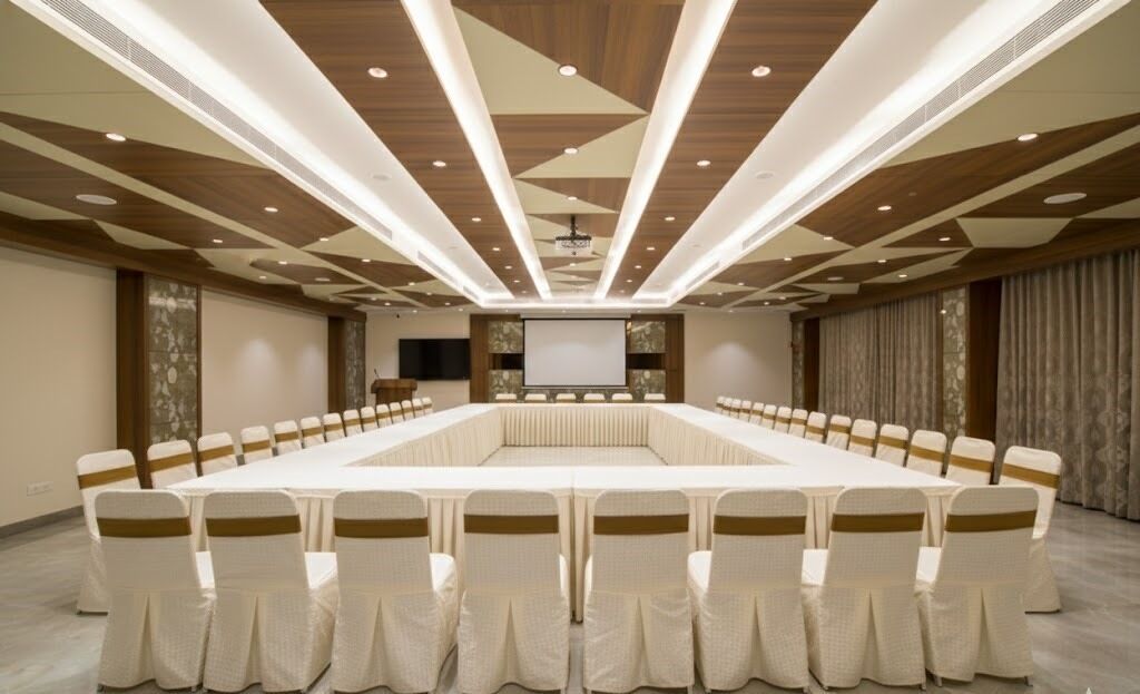 A conference room with a long table, chairs with gold sashes, wooden ceiling panels, and a projector screen.