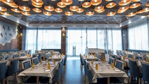 A restaurant with multiple tables set for dining, featuring a modern ceiling design with circular light fixtures. - Hotel Silvera Grand (Ahmedabad)
