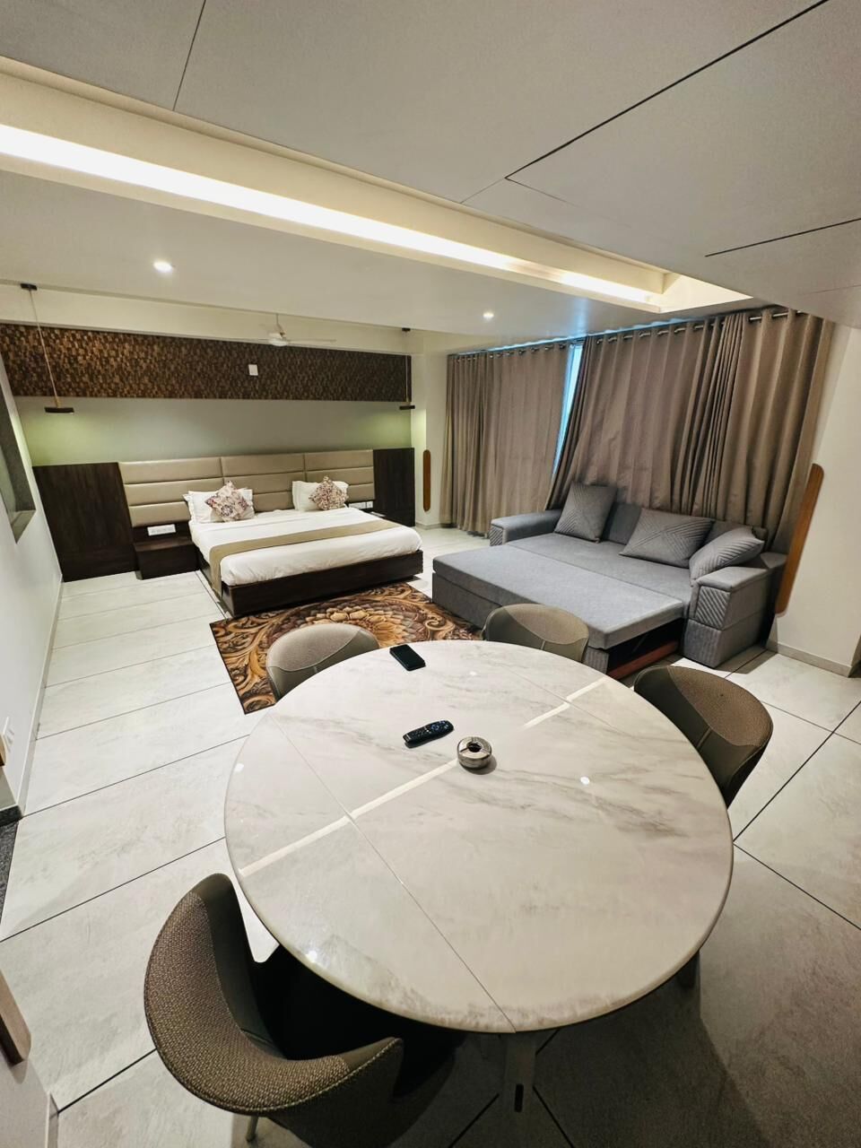 A modern hotel room with a bed, sofa, and a dining area with a table and chairs.