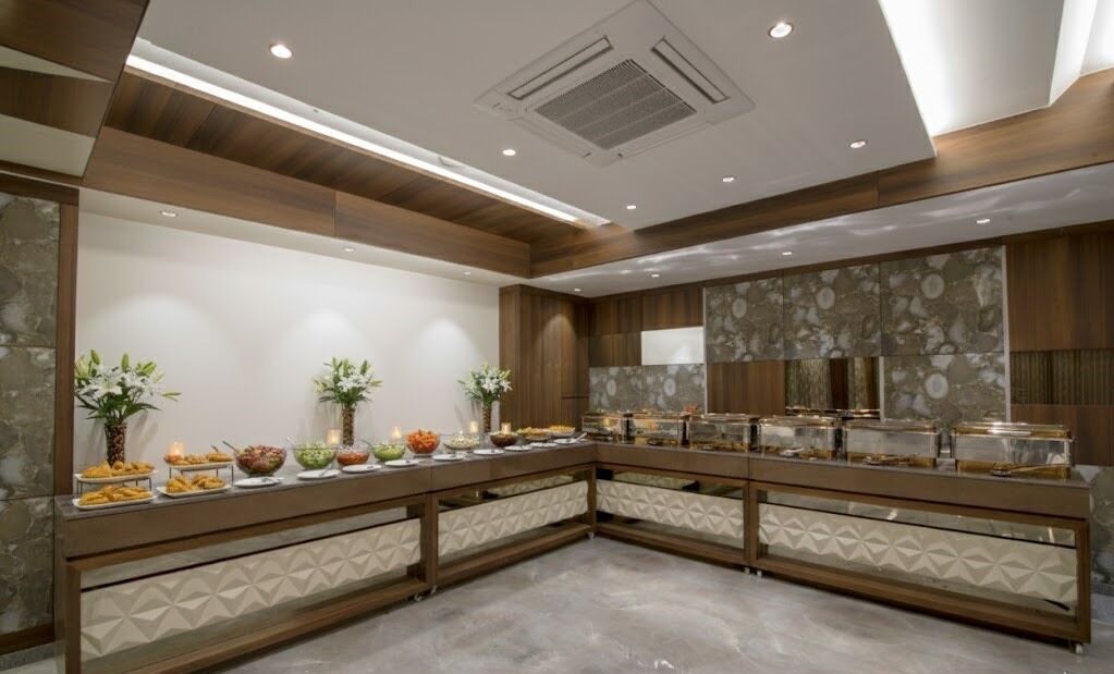 A buffet setup with multiple food stations, a stone wall with a decorative pattern, and a ceiling with recessed lighting.