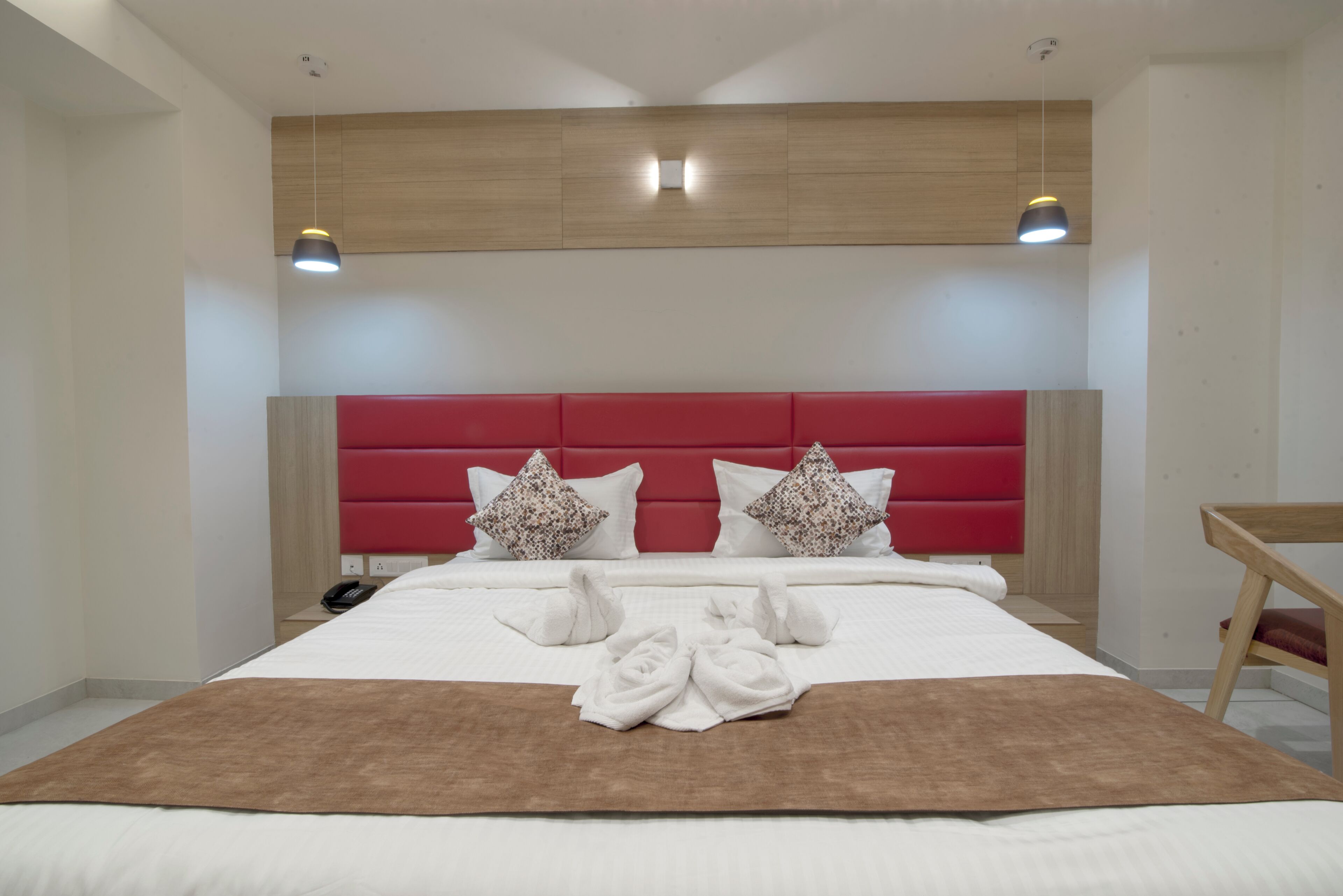 A hotel room with a large bed, red headboard, and two pendant lights.
