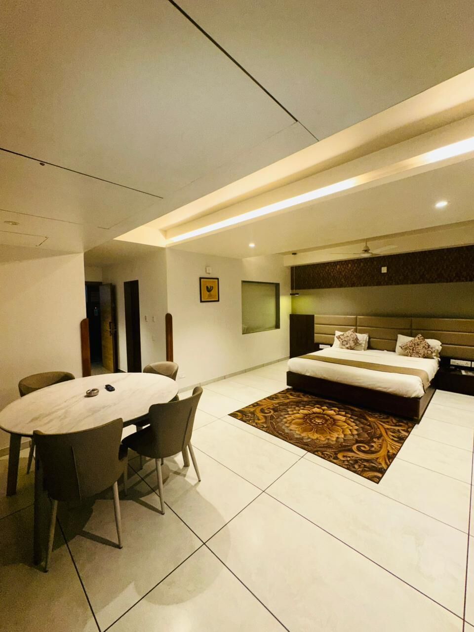 A modern hotel room with a large bed, a dining area with chairs, and a small table.
