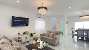 Una sala de estar moderna con un sofá color beige, una mesa de centro de vidrio y un televisor montado en la pared.