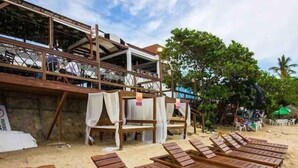 Sillones de madera en una playa arenosa, con un edificio al fondo.