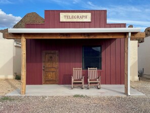 A rustic building with a wooden door marked "18" and two wooden chairs outside. - Ten Bits Ranch - Room # 18 - Telegraph (Terlingua)