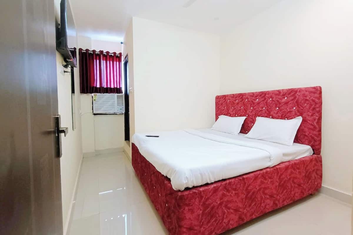 A bedroom with a red bedspread, white pillows, a flat-screen TV mounted on the wall, and a ceiling fan.