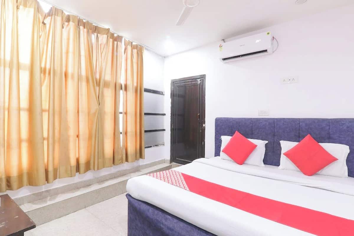 A hotel room with a bed, curtains, an air conditioning unit, and a door.