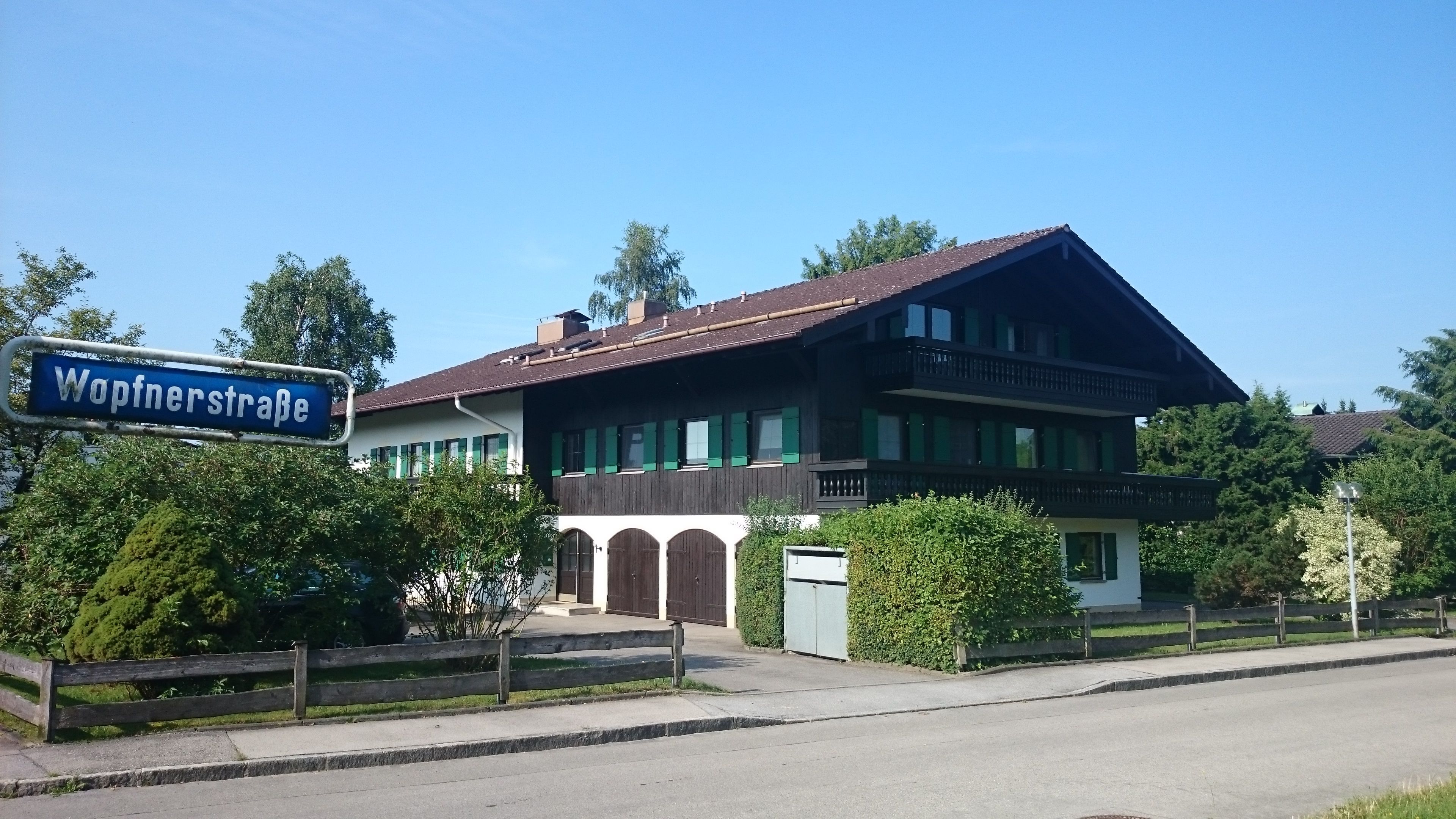 A two-story building with a balcony, a sign indicating 'Wopfnerstraße', and a well-maintained lawn.