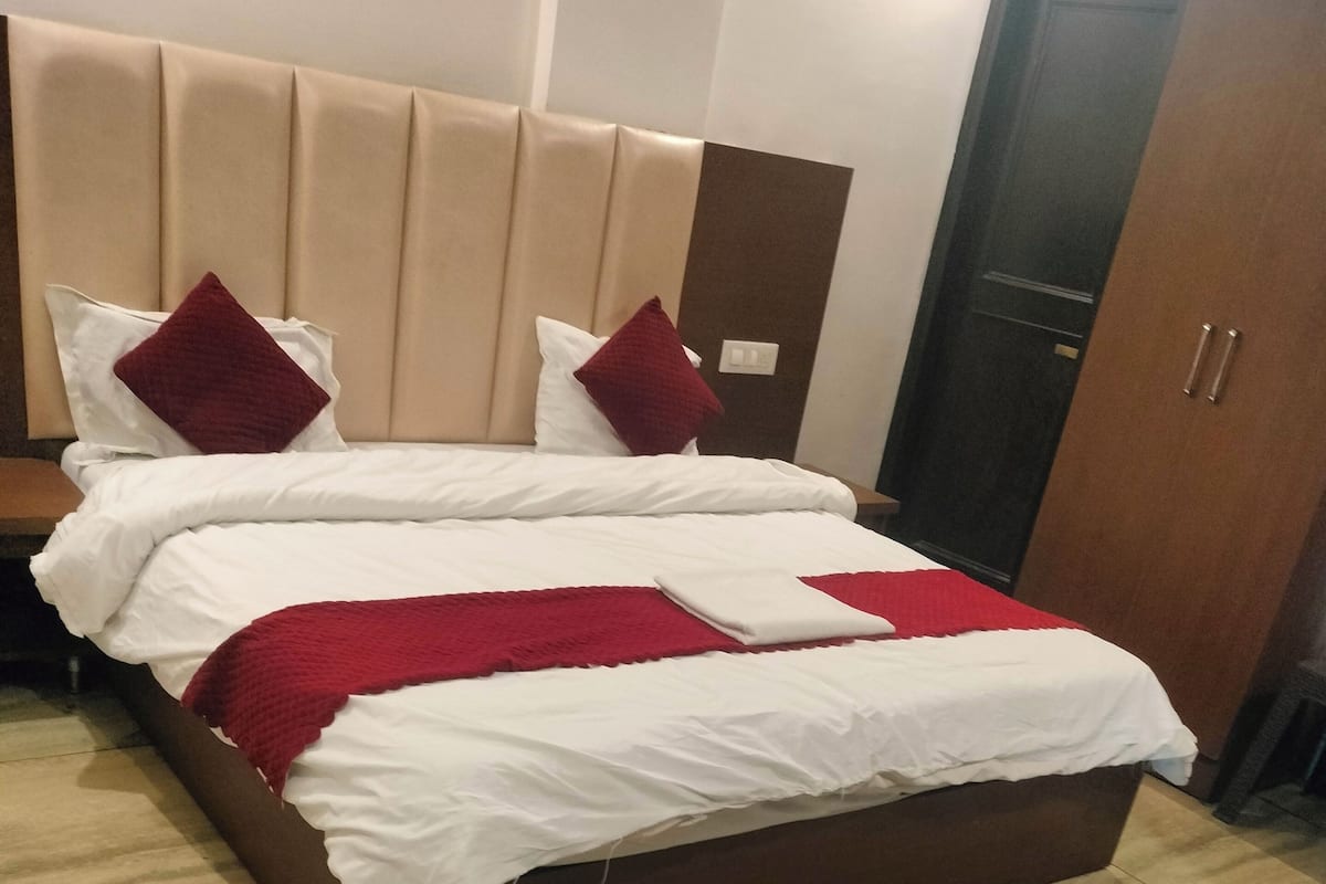 A neatly made bed with white and red bedding, a wooden headboard, and a tiled floor.