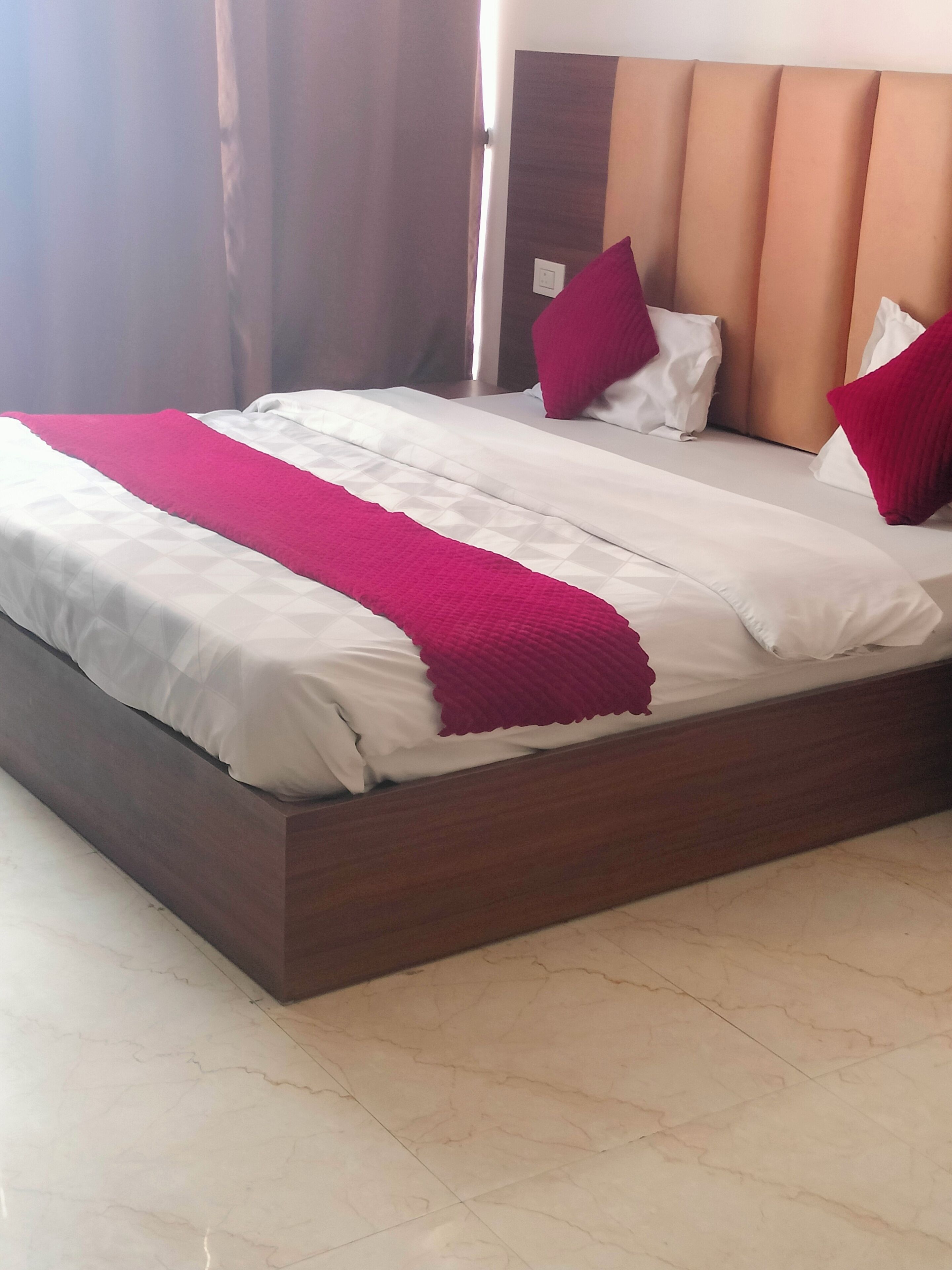 A neatly made bed with white and pink bedding, a wooden headboard, and a marble floor.
