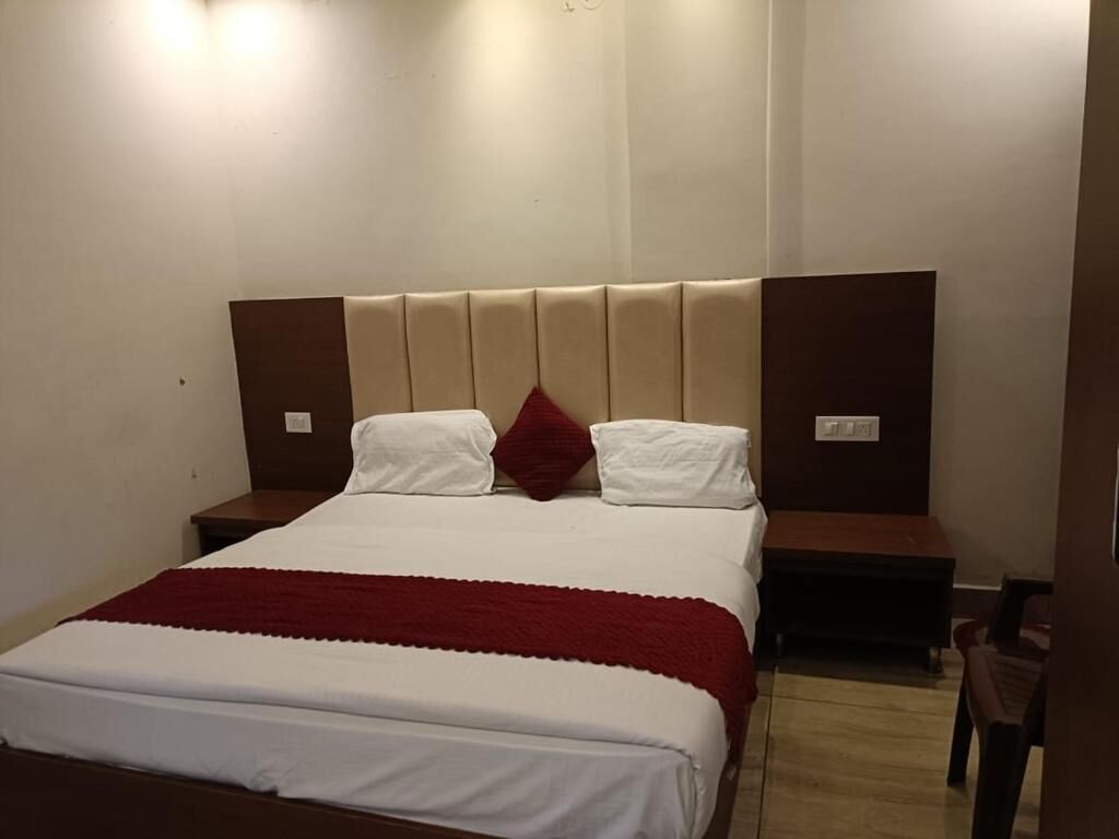 A hotel room with a large bed, two bedside tables, and a red throw blanket.