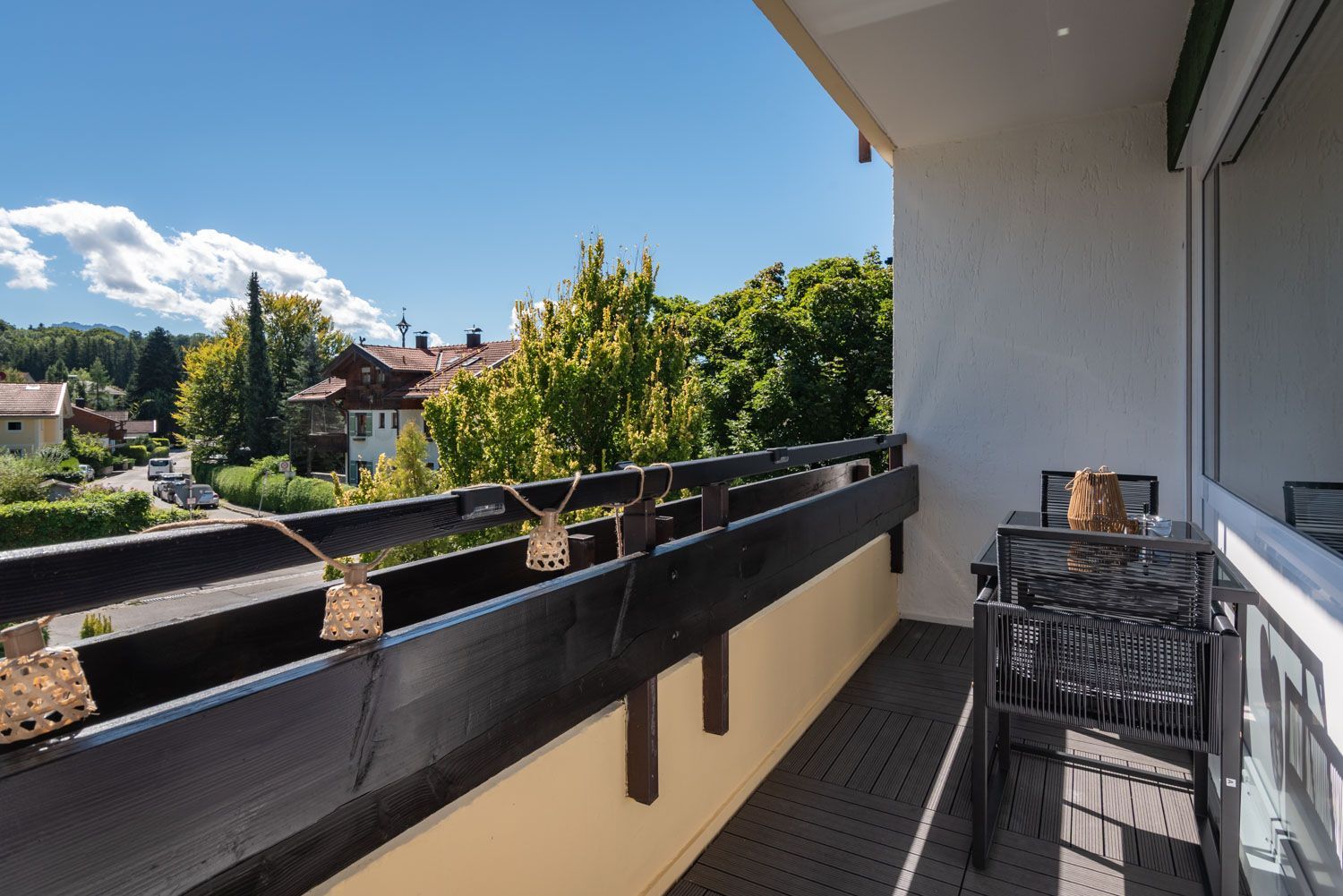 Ein Balkon mit Holzgeländer, einem Tisch mit Stühlen und Blick auf ein Wohngebiet mit Häusern und Bäumen.