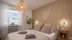 A bedroom with a bed, bedside tables, a hanging light fixture, a macrame wall hanging, and a window with curtains. - MY STAY - Relaxation on Lake Chiemsee in a central location in Prien (Prien am Chiemsee)