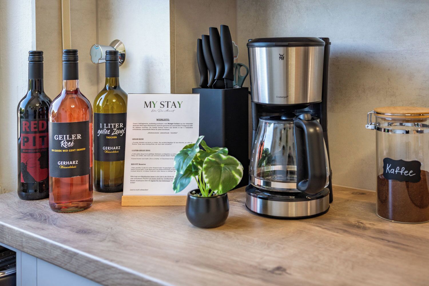 Un comptoir de cuisine avec des bouteilles de vin, une machine à café, un menu et un bocal de café.