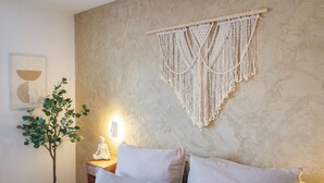 A bedroom with a bed, pillows, a macrame wall hanging, a wall-mounted light, and a small plant. - MY STAY - Relaxation on Lake Chiemsee in a central location in Prien (Prien am Chiemsee)
