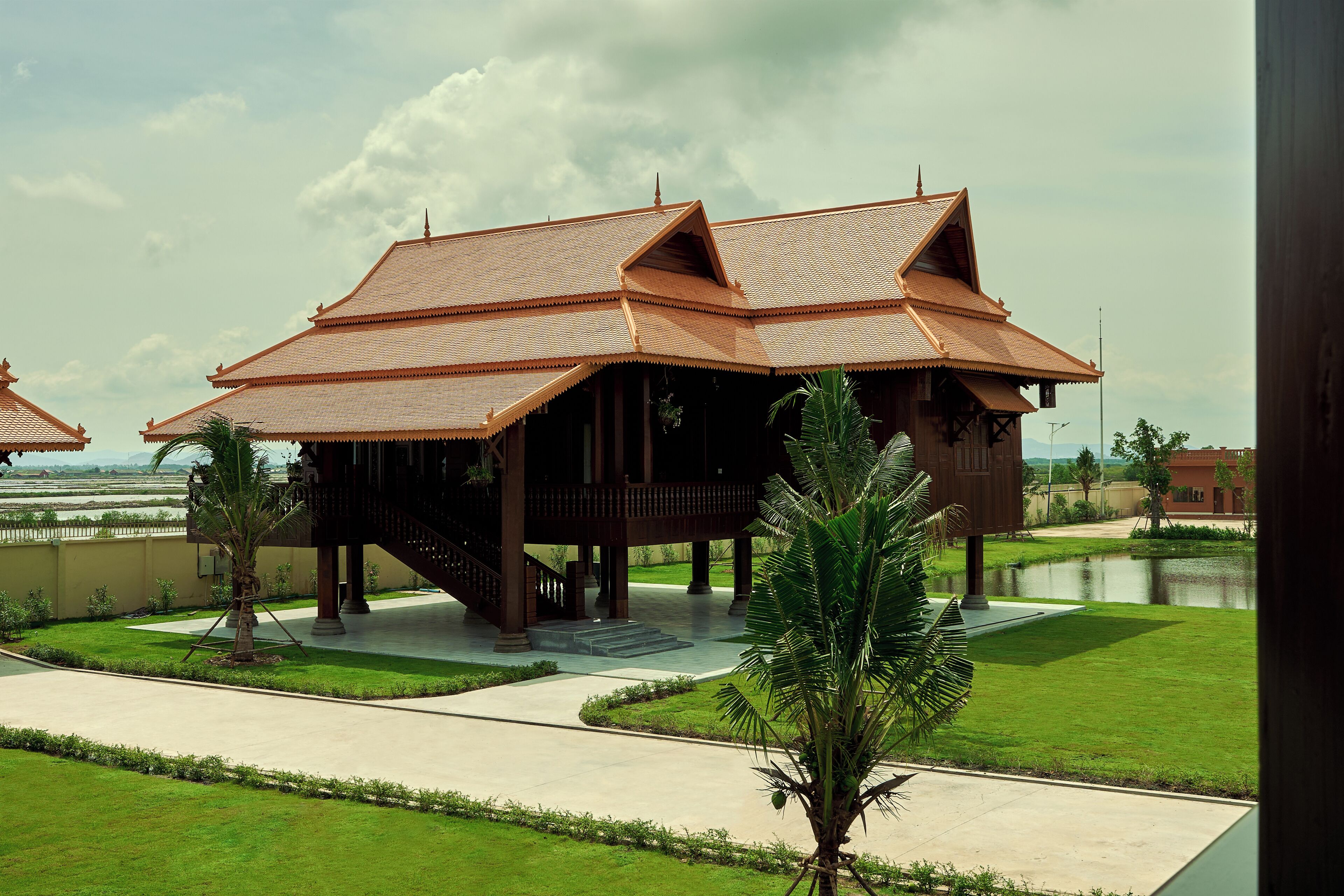 Une construction traditionnelle en bois, dotée d’un toit en tuiles, entourée d’une pelouse bien entretenue et agrémentée d’un élément décoratif aquatique.