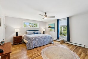 A bedroom with a bed, bedside tables, a ceiling fan, a window with curtains, and a view of greenery outside. - BEACH! 4Bdrm-Fire pit/patio/outdoor shower! (Kennebunk)