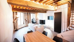 A modern living room with a wooden ceiling, a sofa, a dining table, and a TV mounted on the wall. - Duplex "Le Bourgogne" historic center of Orléans (Orléans)