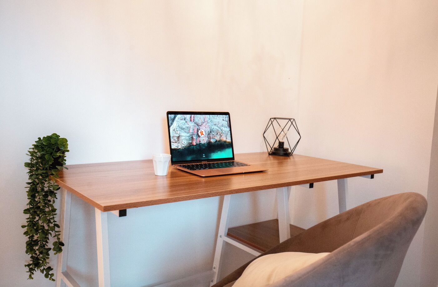 Een houten bureau met een laptop, een witte mok en een decoratief object met een geometrisch patroon.