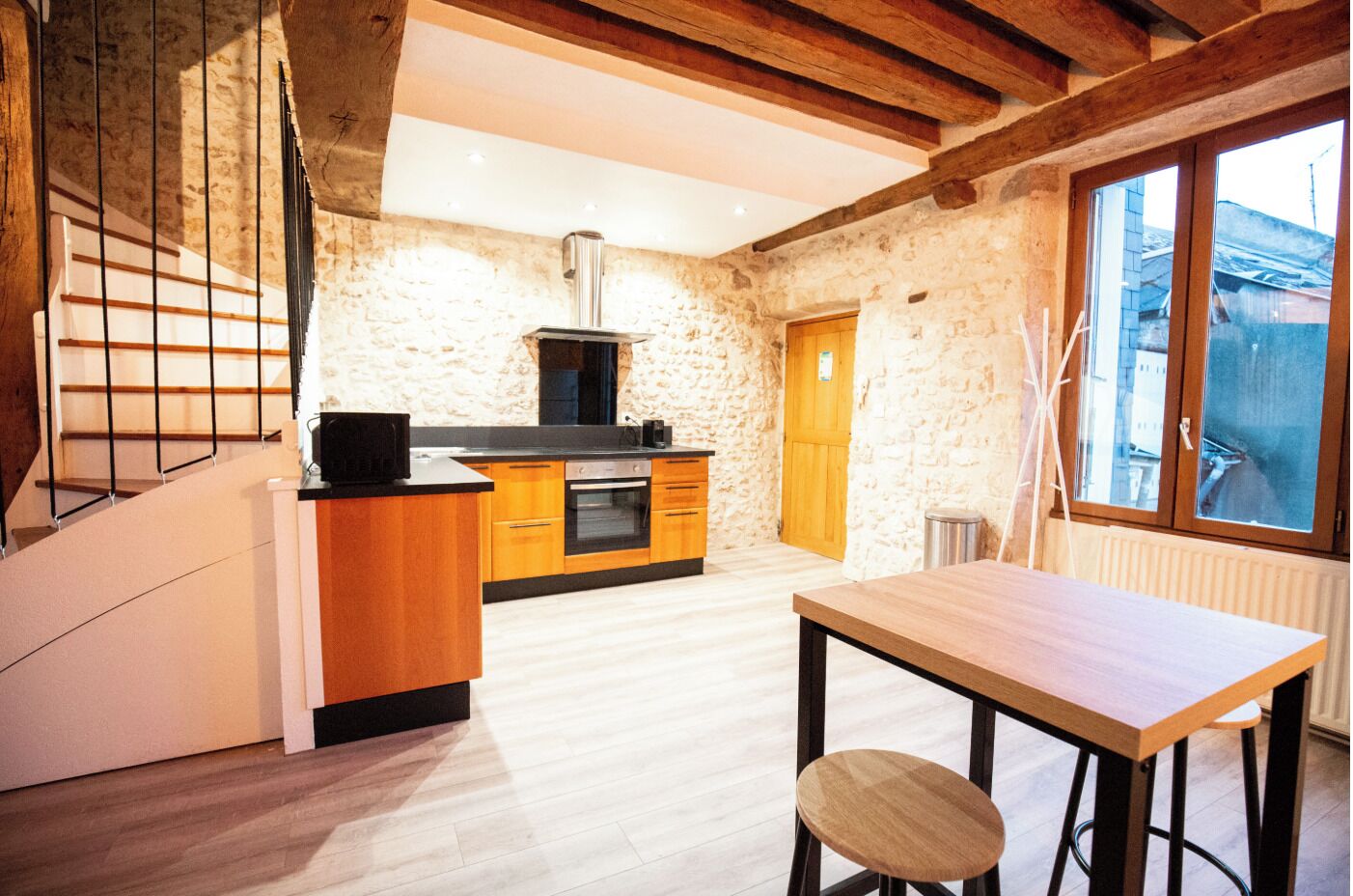 Eine moderne Küche mit Holzschränken, einem eingebauten Ofen und einer schwarzen Mikrowelle. Es gibt einen Essbereich mit einem Holztisch und Stühlen.