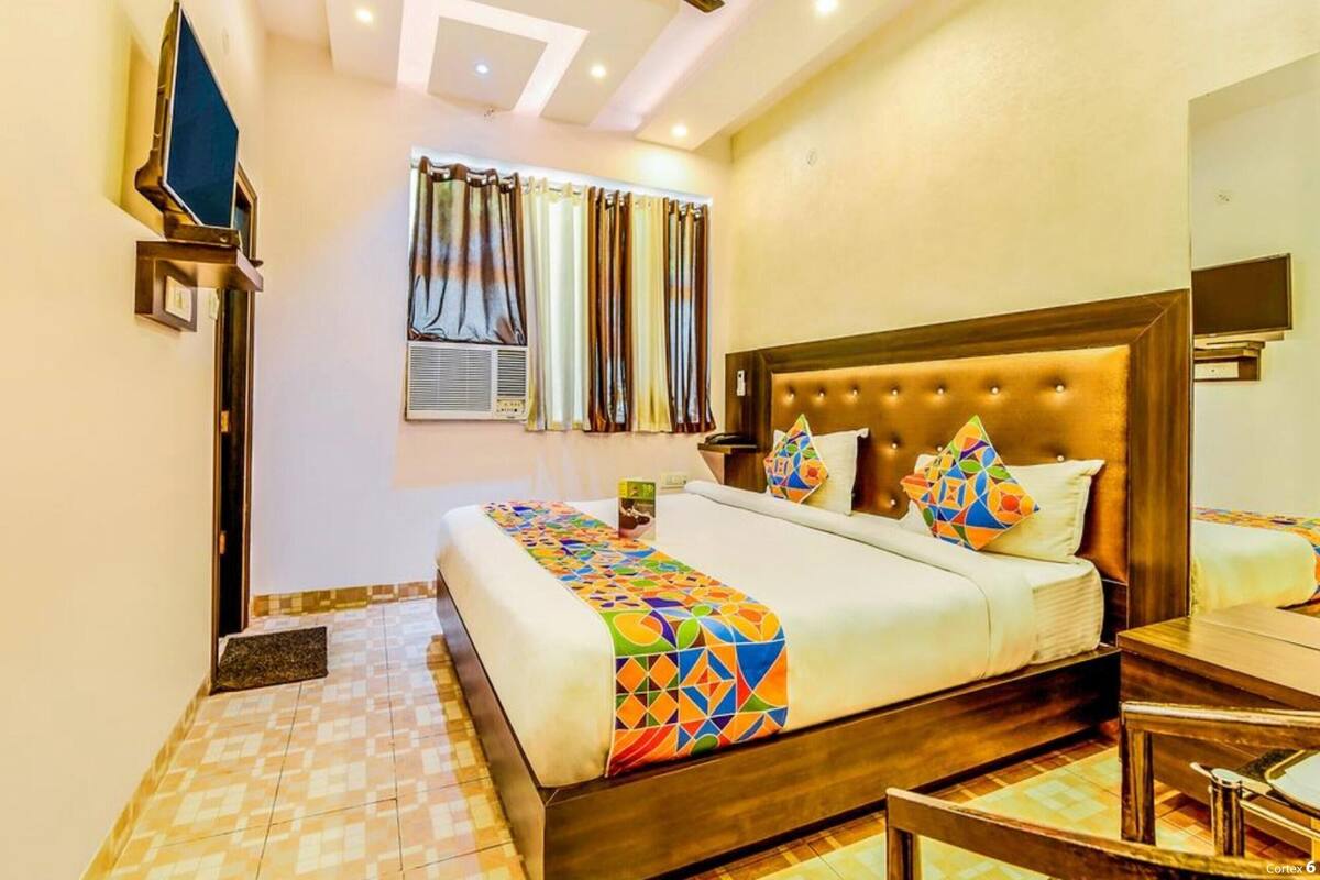 A hotel room with a large bed, a wooden headboard, a bedside table, a mirror, and a television mounted on the wall.