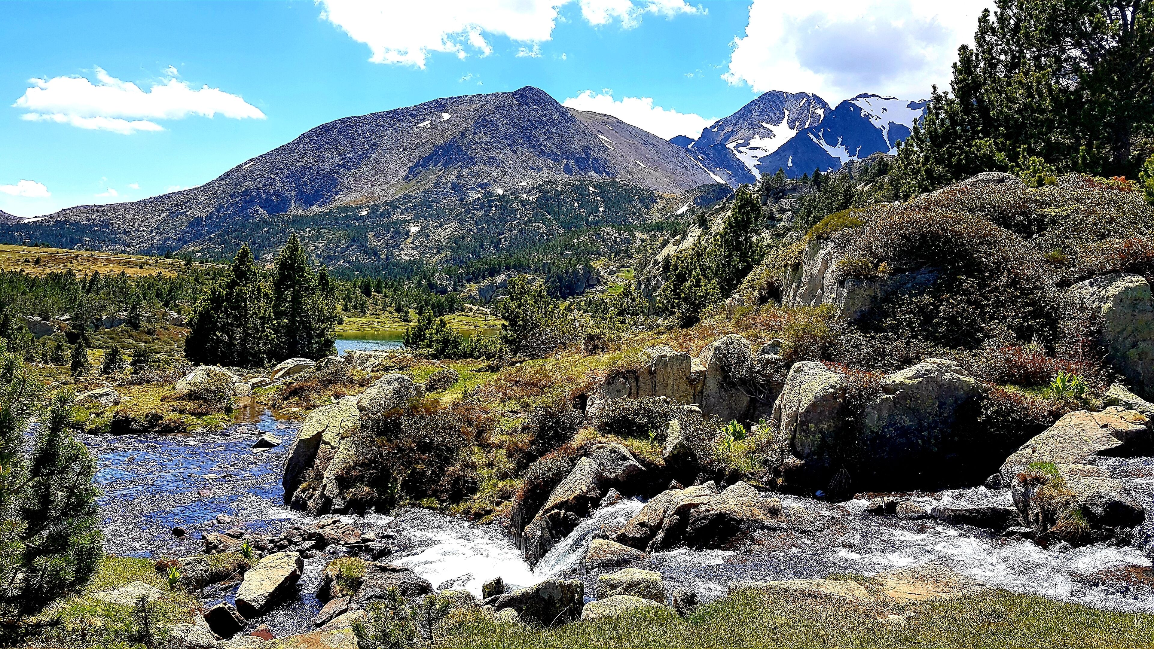 Un paysage montagneux avec un lac aux eaux limpides, un terrain rocheux et une forêt dense.