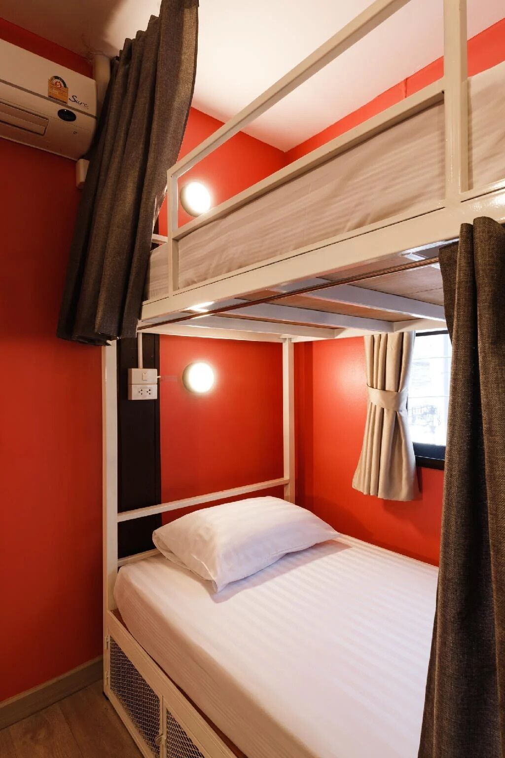 A bunk bed room with a red wall, a window with curtains, and an air conditioning unit.