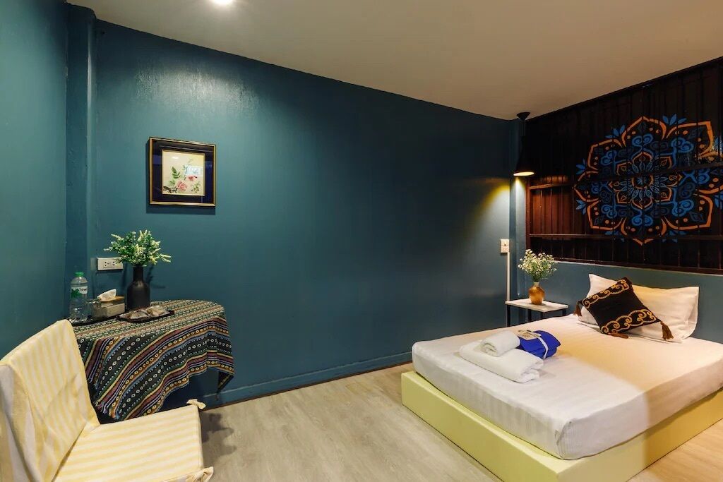 Ein Hotelzimmer mit Bett, Sessel, kleinem Tisch und einer Vase sowie einer Wanddekoration.