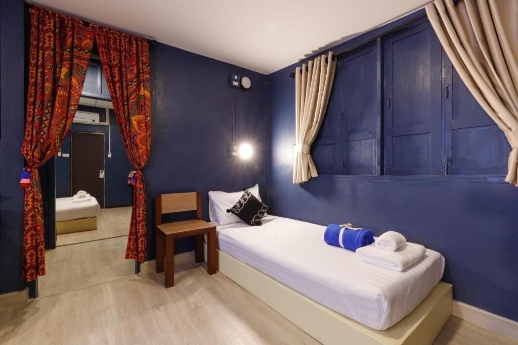 A hotel room with a bed, a chair, a bedside table, a mirror, and a window with curtains.