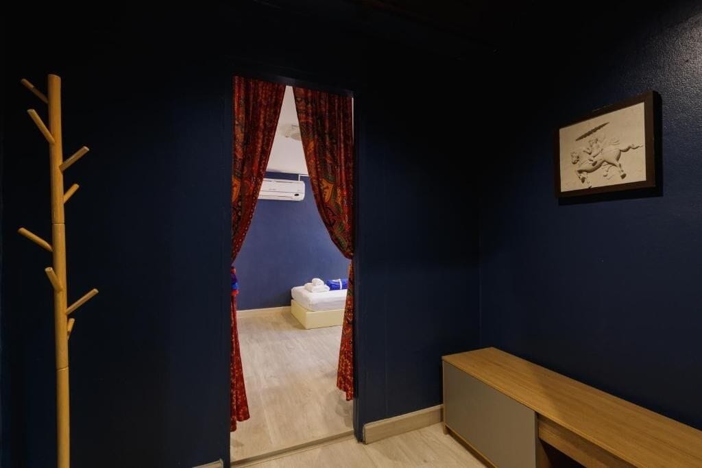 A hotel room with a dark blue wall, a wooden bench, a bed with white bedding, and a framed picture on the wall.
