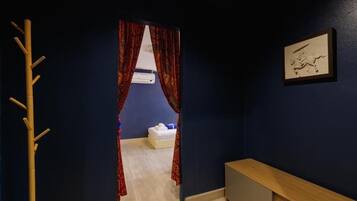 A hotel room with a dark blue wall, a wooden bench, a bed with white bedding, and a framed picture on the wall.