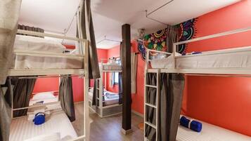 A dormitory room with bunk beds, a colorful tapestry on the wall, and a small window.