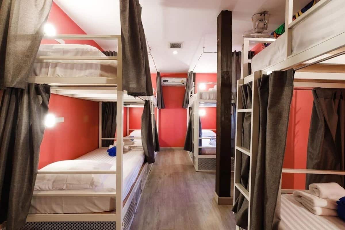 A dormitory room with bunk beds, a central walkway, and a wardrobe with hanging clothes.