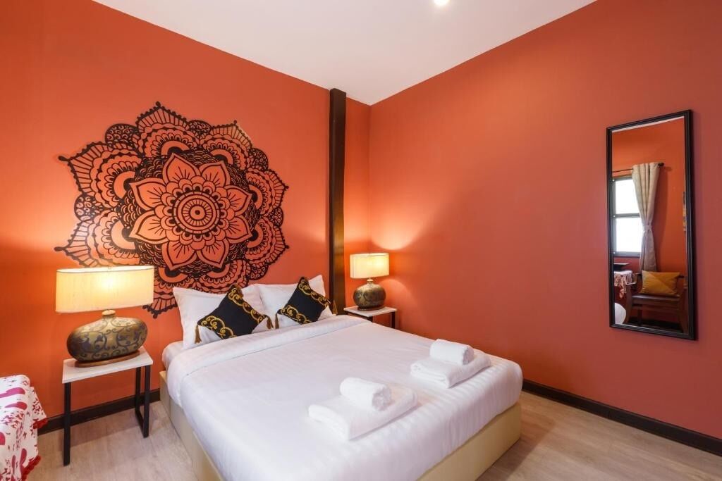 Habitación de hotel con un gran cuadro de mandala en la pared, una cama con ropa blanca, dos mesitas de noche con lámparas y un espejo en la pared.