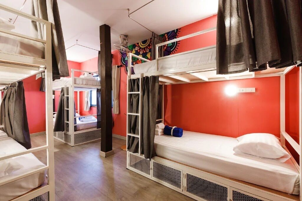 Une chambre de dortoir avec des lits superposés, un mur rouge et un ventilateur de plafond.