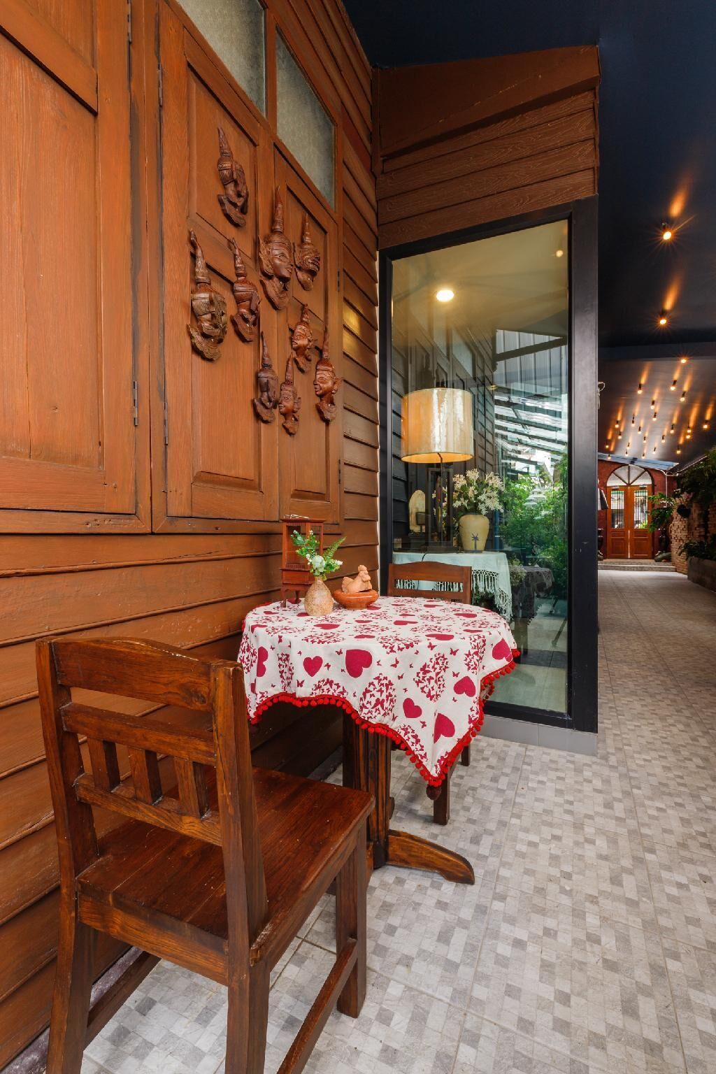 A wooden exterior wall with carved figures, a table with a heart-patterned tablecloth, and a chair.