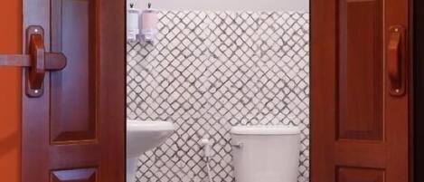 Eine geöffnete Holztür, die zu einem Badezimmer mit Toilette, Waschbecken und gemusterten Wandfliesen führt.