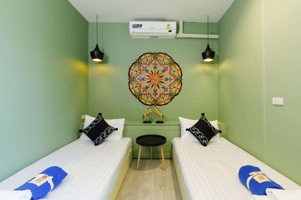 A room with two beds, a small table, a decorative wall piece, and an air conditioning unit.