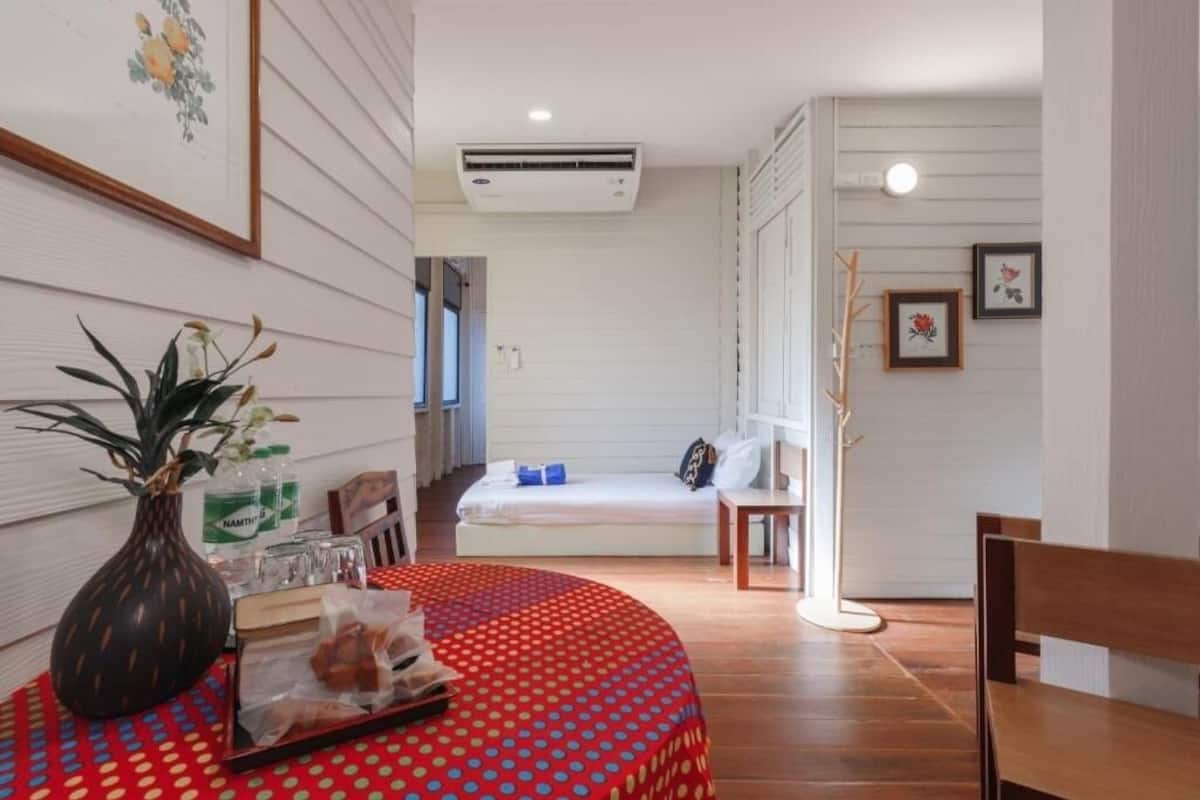 A hotel room with a bed, a small table with a vase and snacks, a wooden bench, and a wall-mounted air conditioner.
