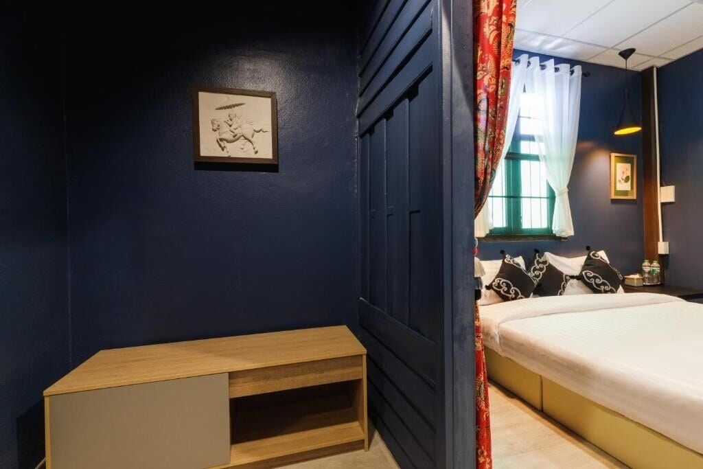A bedroom with a bed, a wooden nightstand, a framed picture on the wall, and a window with curtains.
