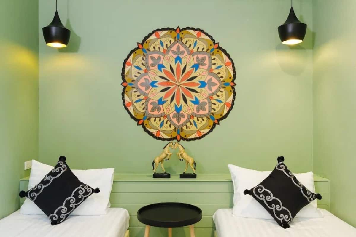 A room with two beds, a round table, and a large decorative wall hanging.