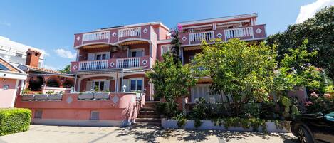 A multi-story pink building with balconies, a staircase, and a garden area.