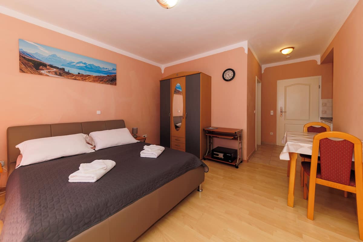 A bedroom with a bed, a desk, a chair, a wardrobe, a clock, and a painting on the wall.