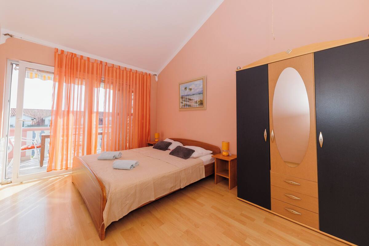 A bedroom with a bed, a wardrobe, a nightstand, and a painting on the wall.
