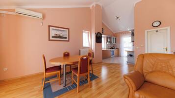 A dining area with a round table and chairs, a kitchen in the background, and a living room with a sofa.
