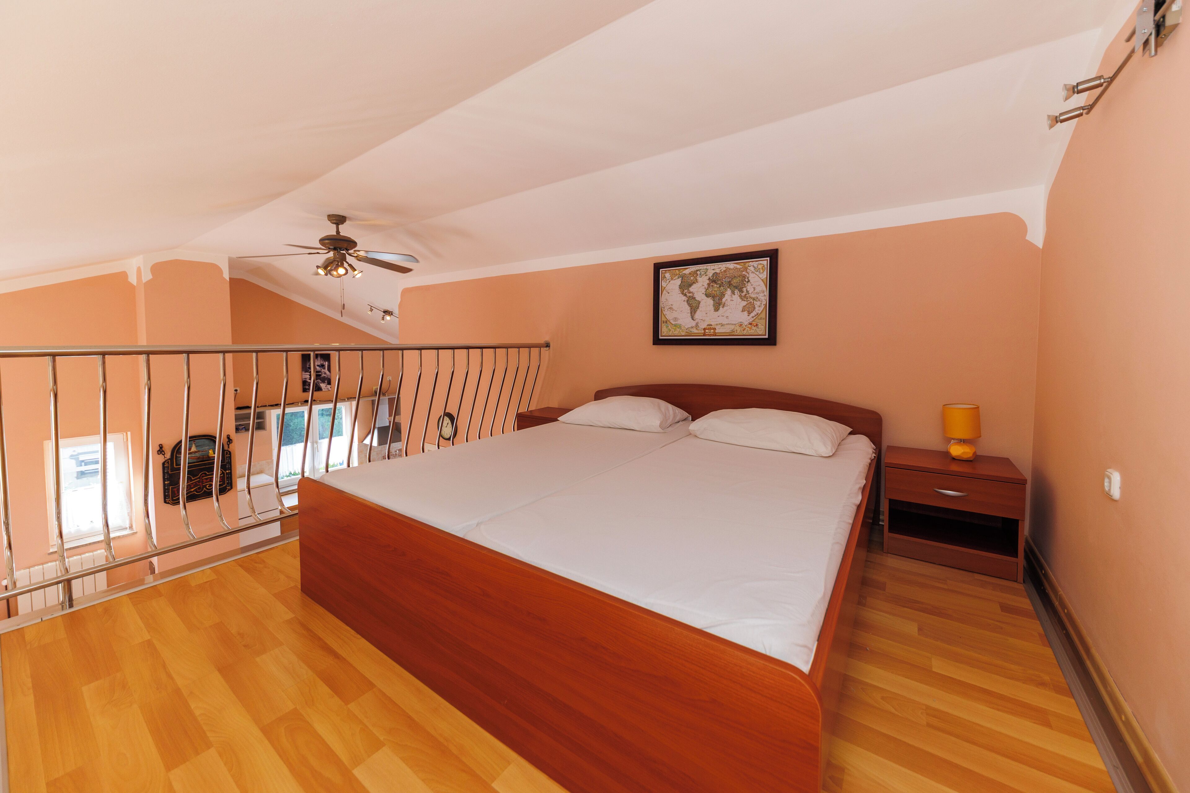 Ein Schlafzimmer mit einem hölzernen Bett, einem Nachttisch, einer Lampe, einem Deckenventilator und einer an der Wand aufgehängten Weltkarte.