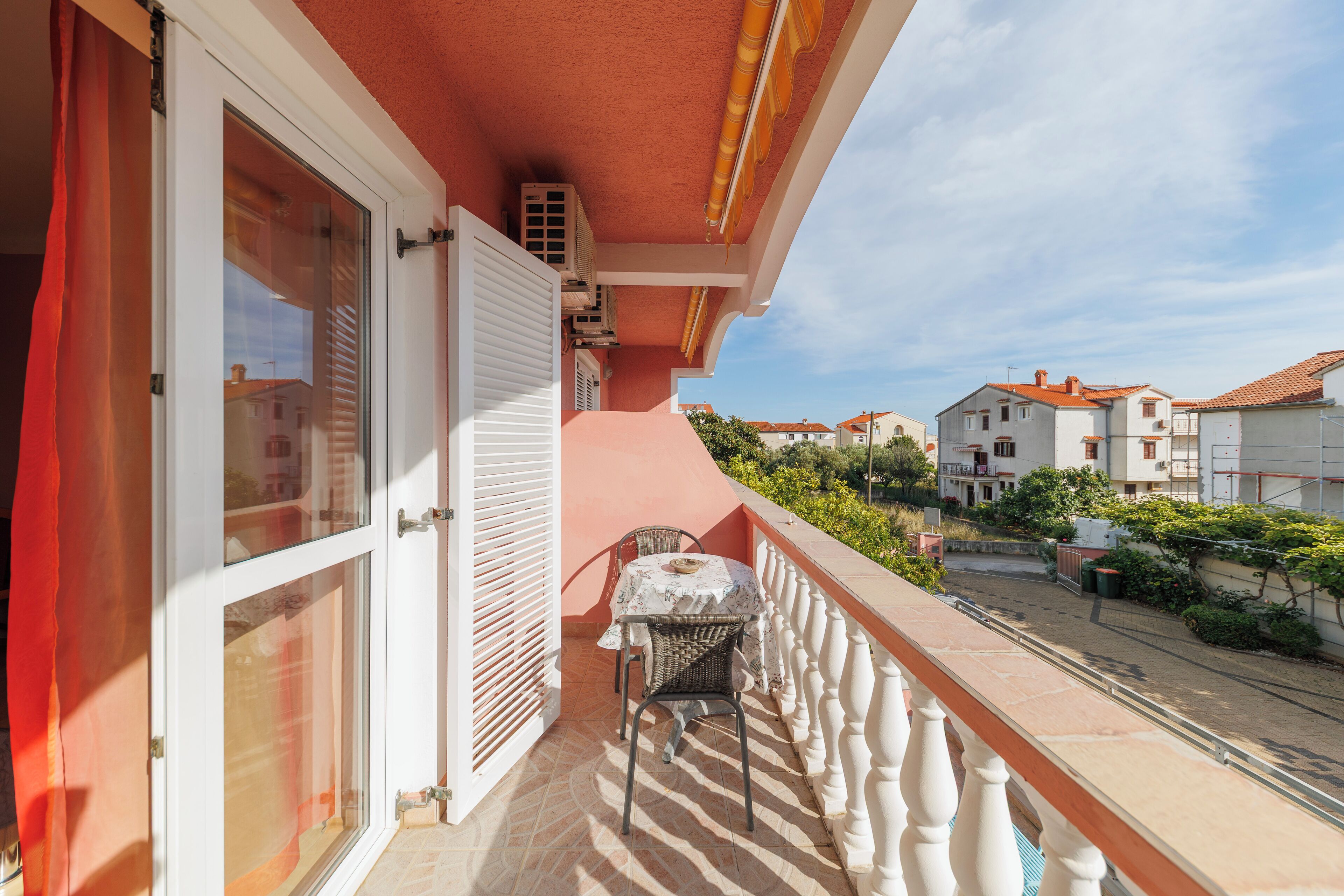 Un balcon avec une table et des chaises, une balustrade blanche et une vue sur les bâtiments voisins.