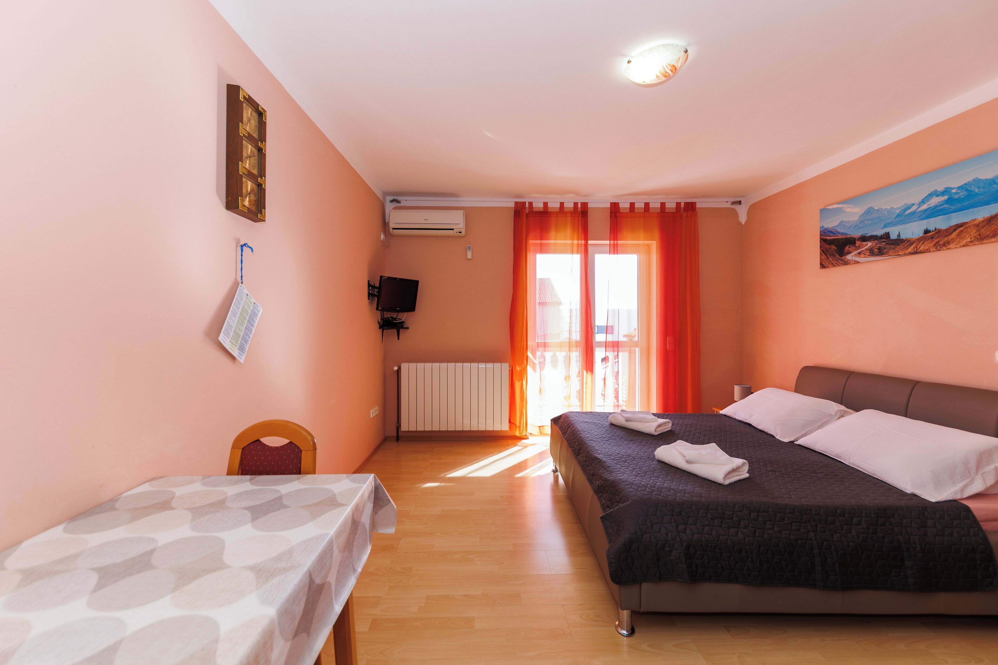 A bedroom with a bed, a table, a chair, a painting, and a window with curtains.